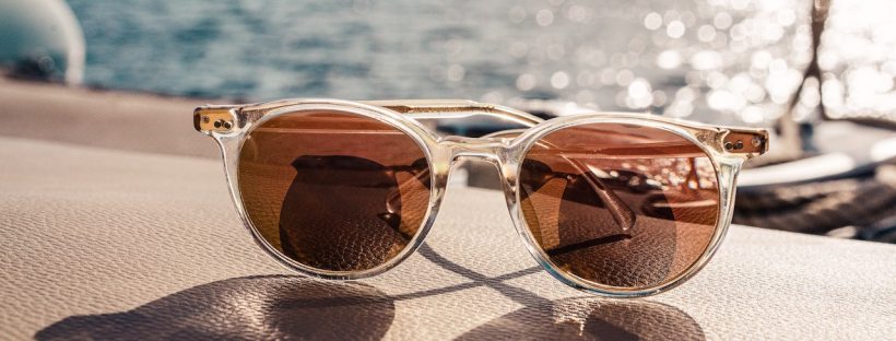 Sunglasses are propped on a surface. Out of focus in the background is the ocean.