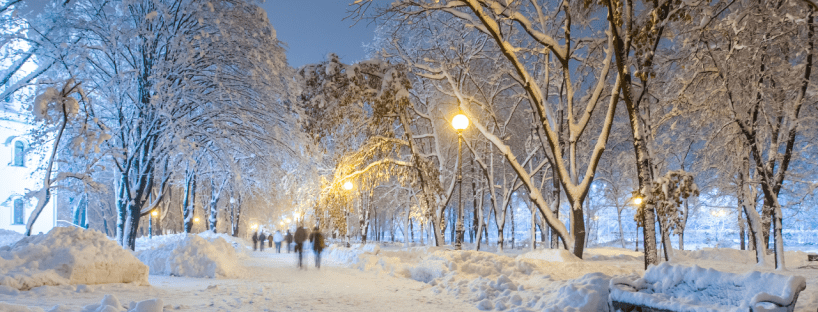 A pathway is covered in snow at twilight. Out of focus, people are walking away from the camera.