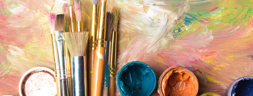 Used-but-clean paintbrushes sit on an abstract painted canvas with open paint pots