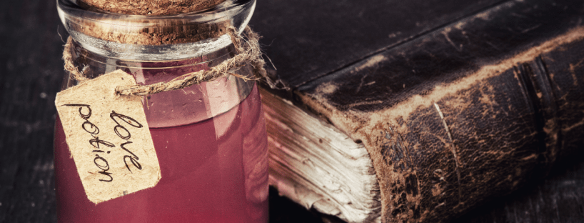 A love potion sits beside a weathered leather book on a table