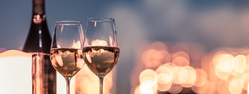 Two glasses of wine with a bottle sit at the forefront with soft, blurred lighting in the background