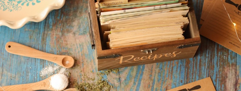 Recipe cards and wooden measuring implements sit on a faded blue wood tabletop