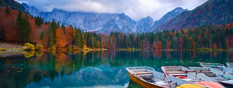 Boats sit on a calm lake in fall with mountains behind them