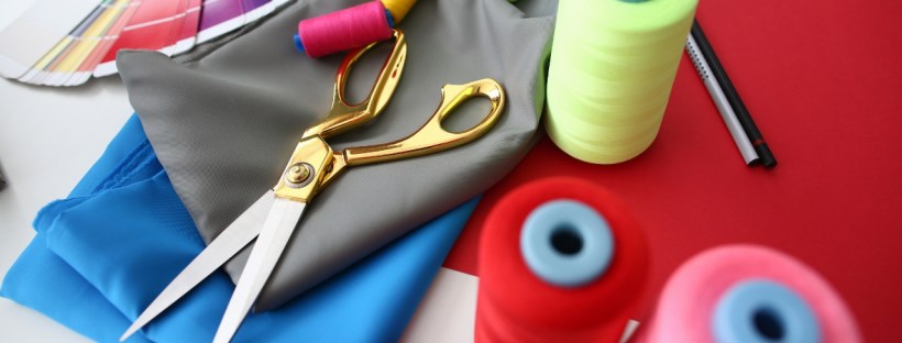 A pair of gold scissors sits on some fabric with spools of thread and a colour wheel