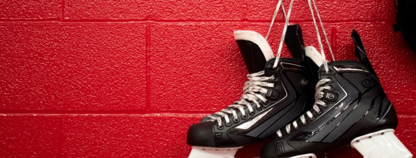 Hockey skates are hanging on a hook in a dressing room with red walls