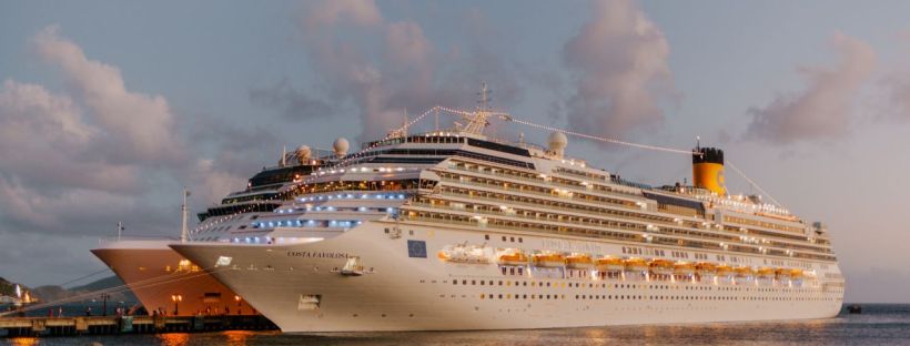 A cruise ship lit up at dusk docked at a port